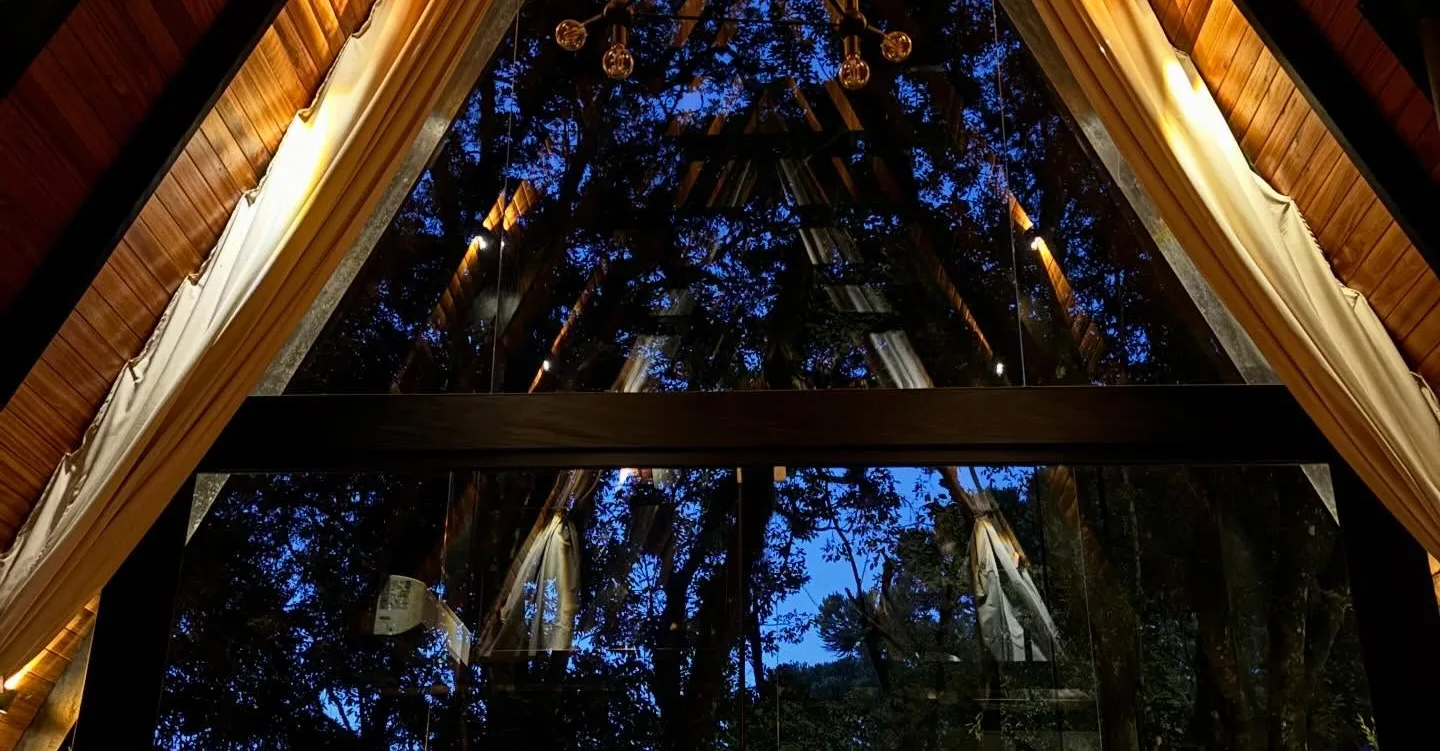 Interior da cabana à noite, com a parede de vidro em A aberta para as árvores