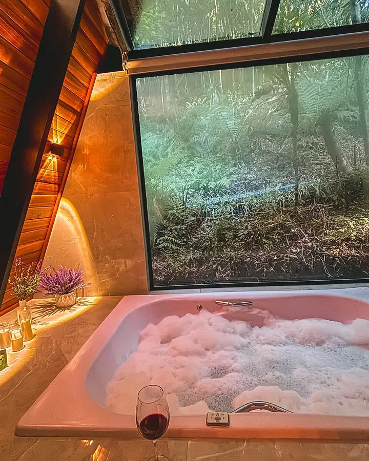 Banheira de hidromassagem com espuma, diante da janela para a mata