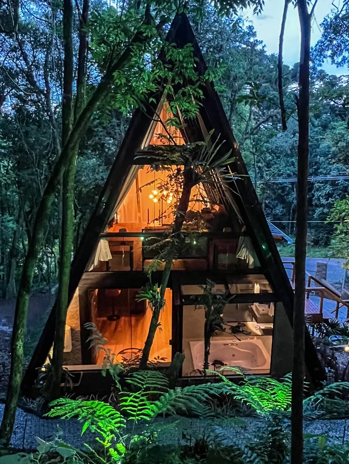 A fachada em A iluminada ao anoitecer, entre samambaias