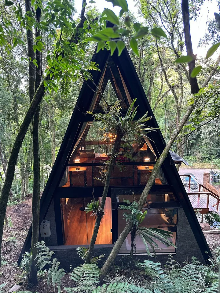 A fachada em A da cabana, com as janelas de vidro, entre as árvores